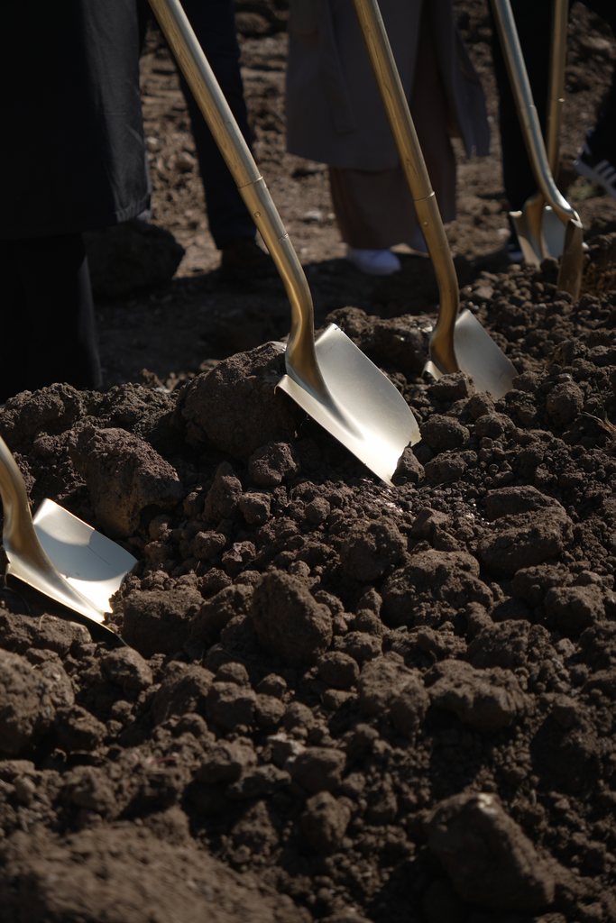 Gold ceremonial shovels driven into dark, freshly turned soil.