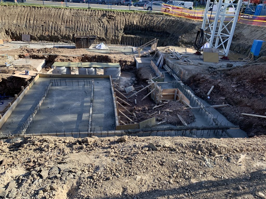 A rectangular concrete footing poured inside timber formwork, steel bars along its edges, with more forms beside it and the crane mast at the right.